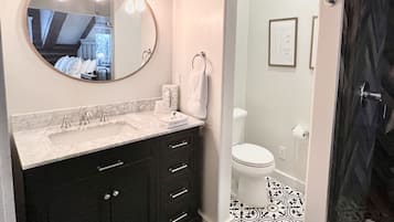 A bathroom with a round mirror, a sink with a marble countertop, dark cabinets, and a patterned floor.