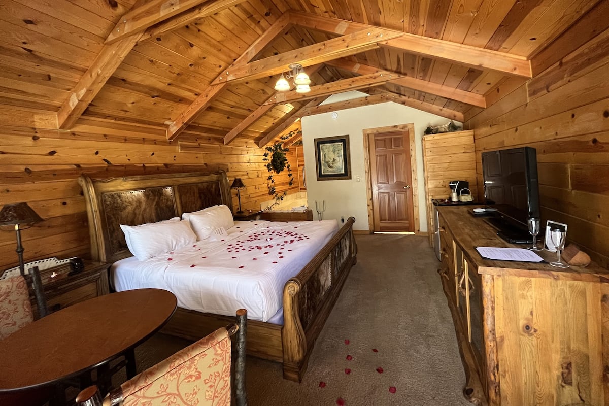 A wooden cabin bedroom with a bed, a desk, a chair, and a television.