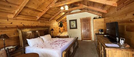 A wooden cabin bedroom with a bed, a desk, a chair, and a television.