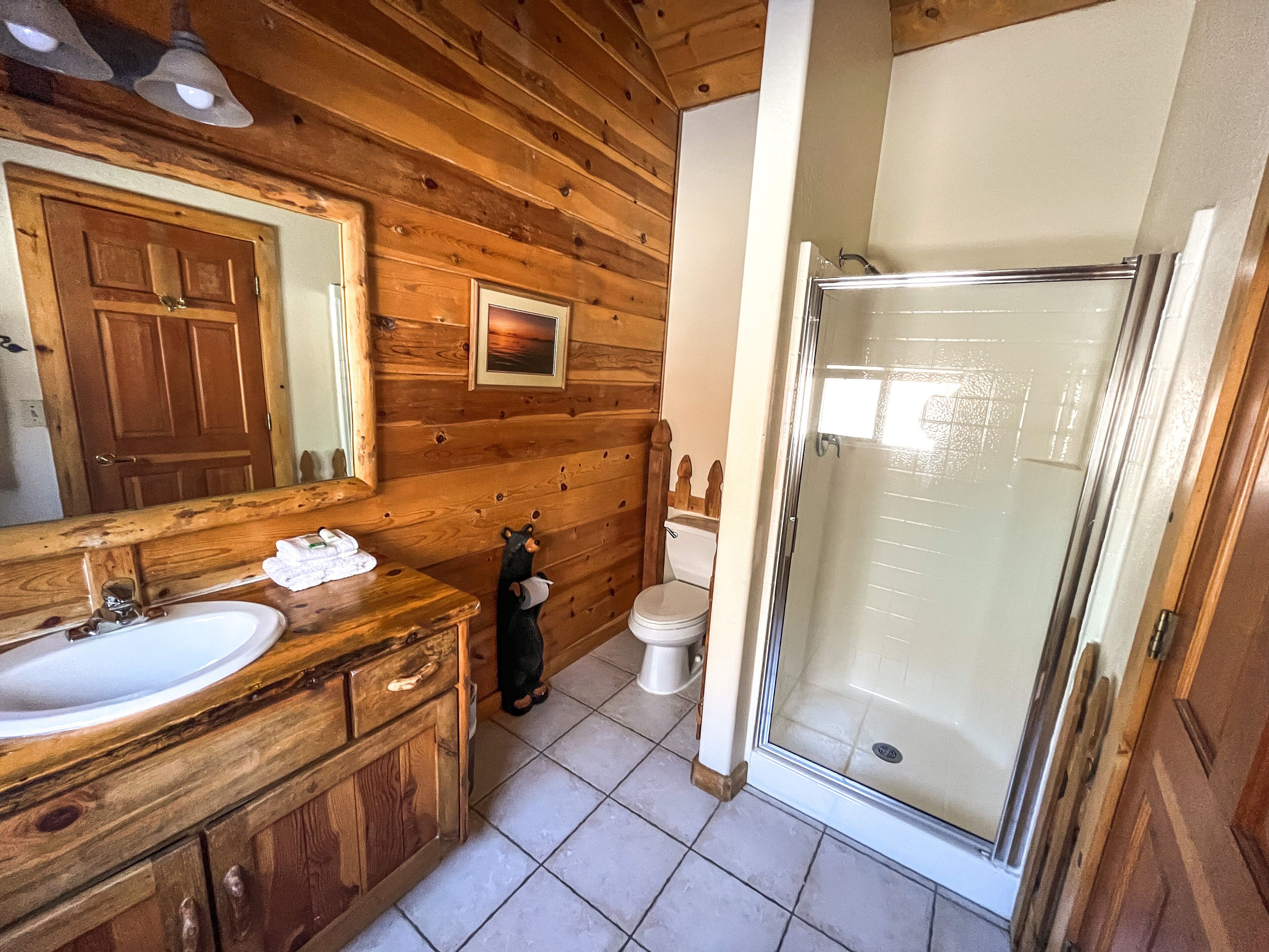 A wooden cabin bathroom with a sink, mirror, toilet, and glass shower enclosure.
