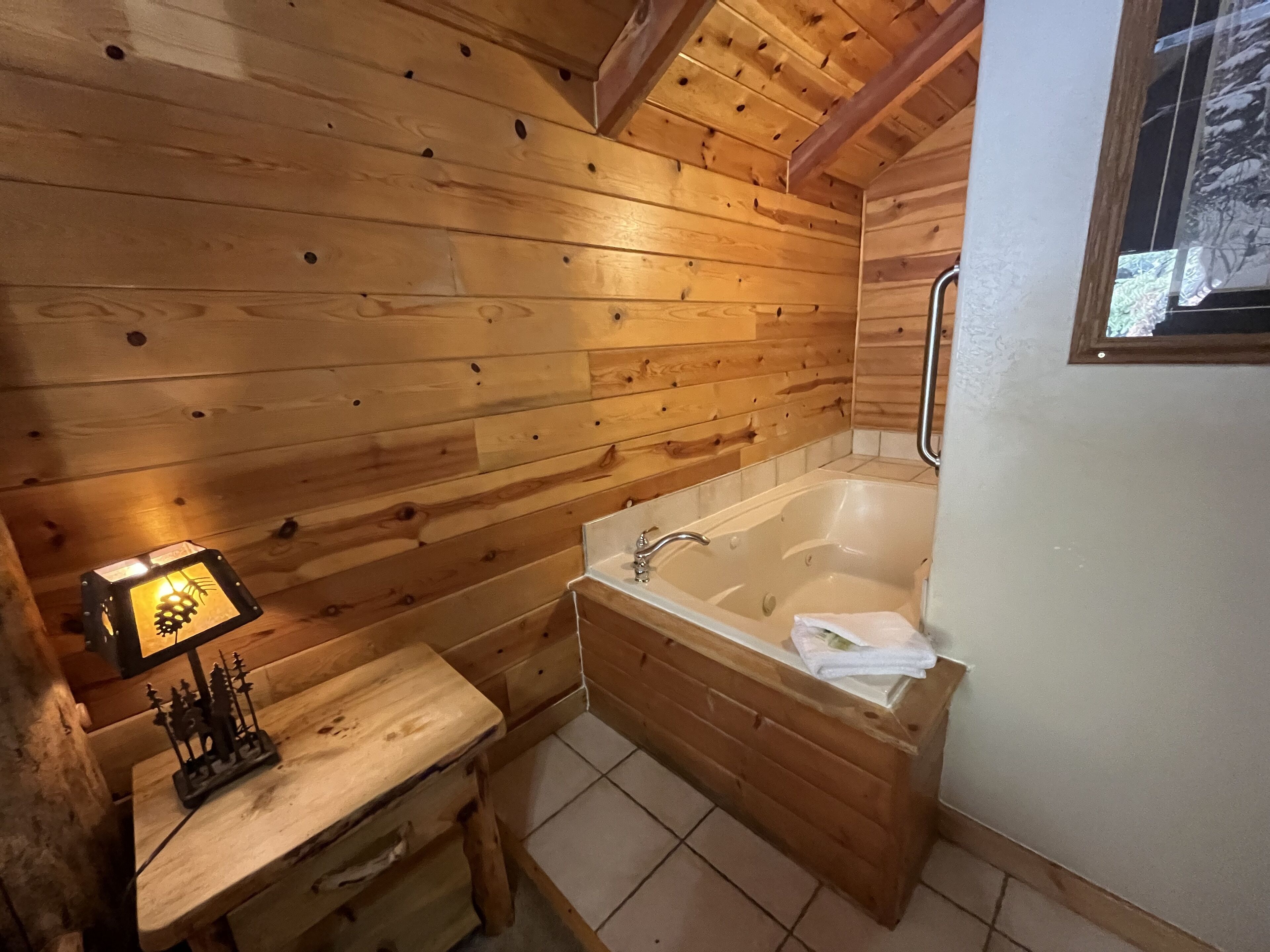 Une salle de bain rustique, avec des murs en bois, comprenant une baignoire, un banc et une petite table agrémentée d’un objet décoratif.