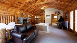 A log cabin interior with a fireplace, a leather sofa, a dining area, and a kitchen. - Alaskan Inn (Ogden)