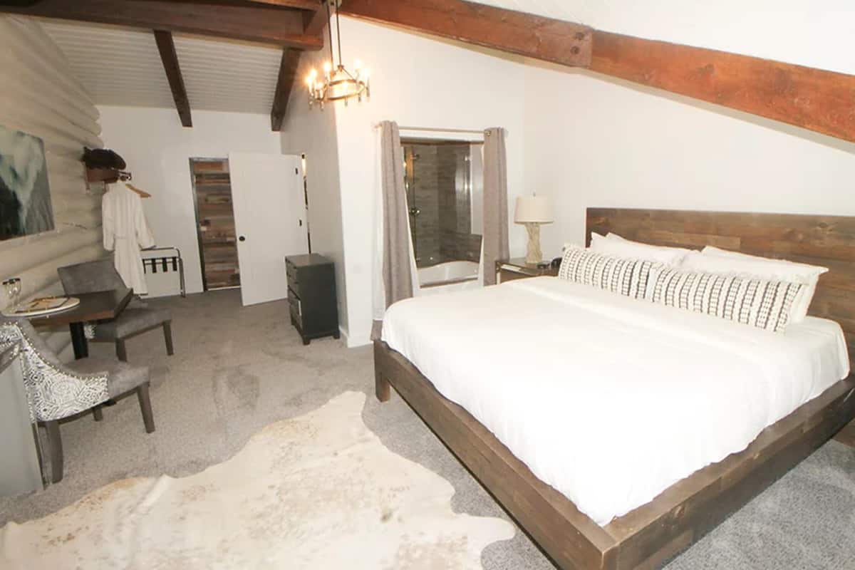 A bedroom with a wooden bed, a desk, a chair, a lamp, and a door leading to a bathroom.