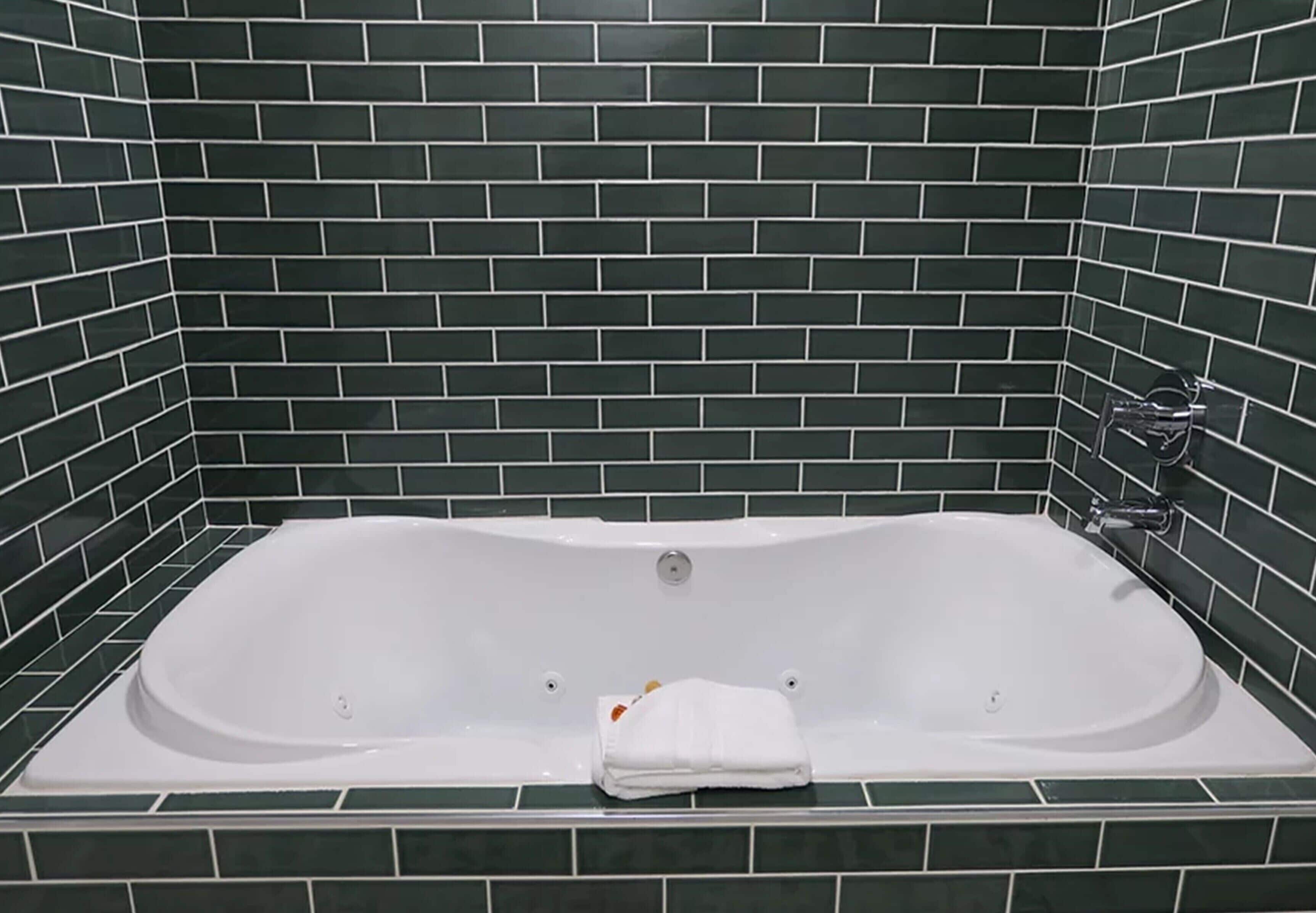 A bathtub with a white interior, surrounded by dark green tiled walls.