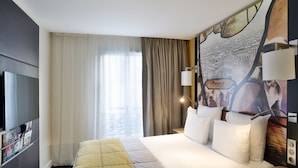 Een hotelkamer met een groot bed, een televisie, een raam met gordijnen en een muur met een stadsgezichtsmural.