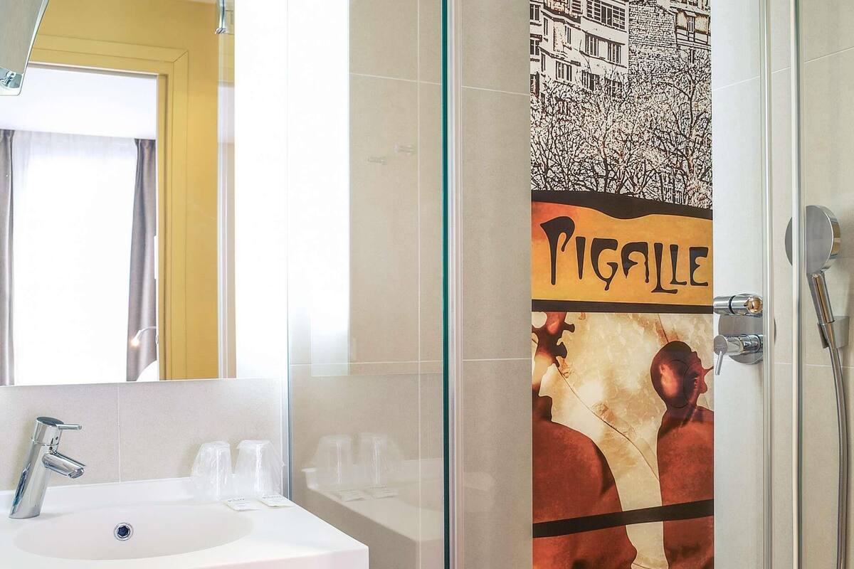 A bathroom with a white sink, a glass shower enclosure, and a poster on the wall.