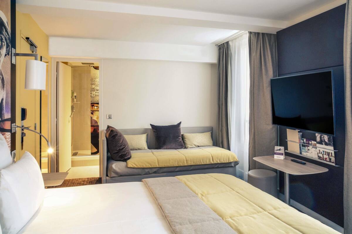 A hotel room with two beds, a TV, a small table, and a bathroom visible through an open door.