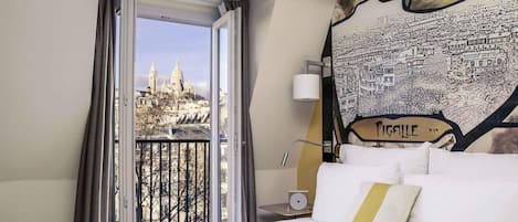 A hotel room with a bed, a window with curtains, a cityscape view, and a wall with a cityscape mural.