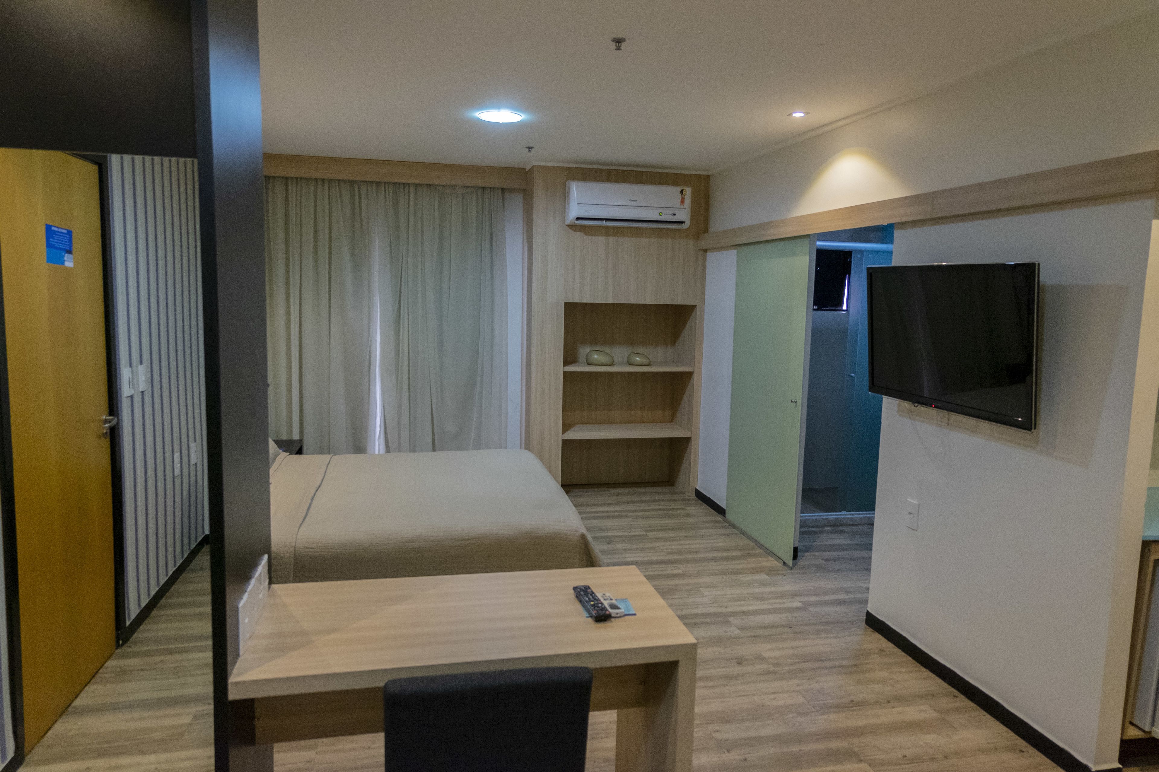 Et hotelværelse med seng, skrivebord, fjernsyn og aircondition.