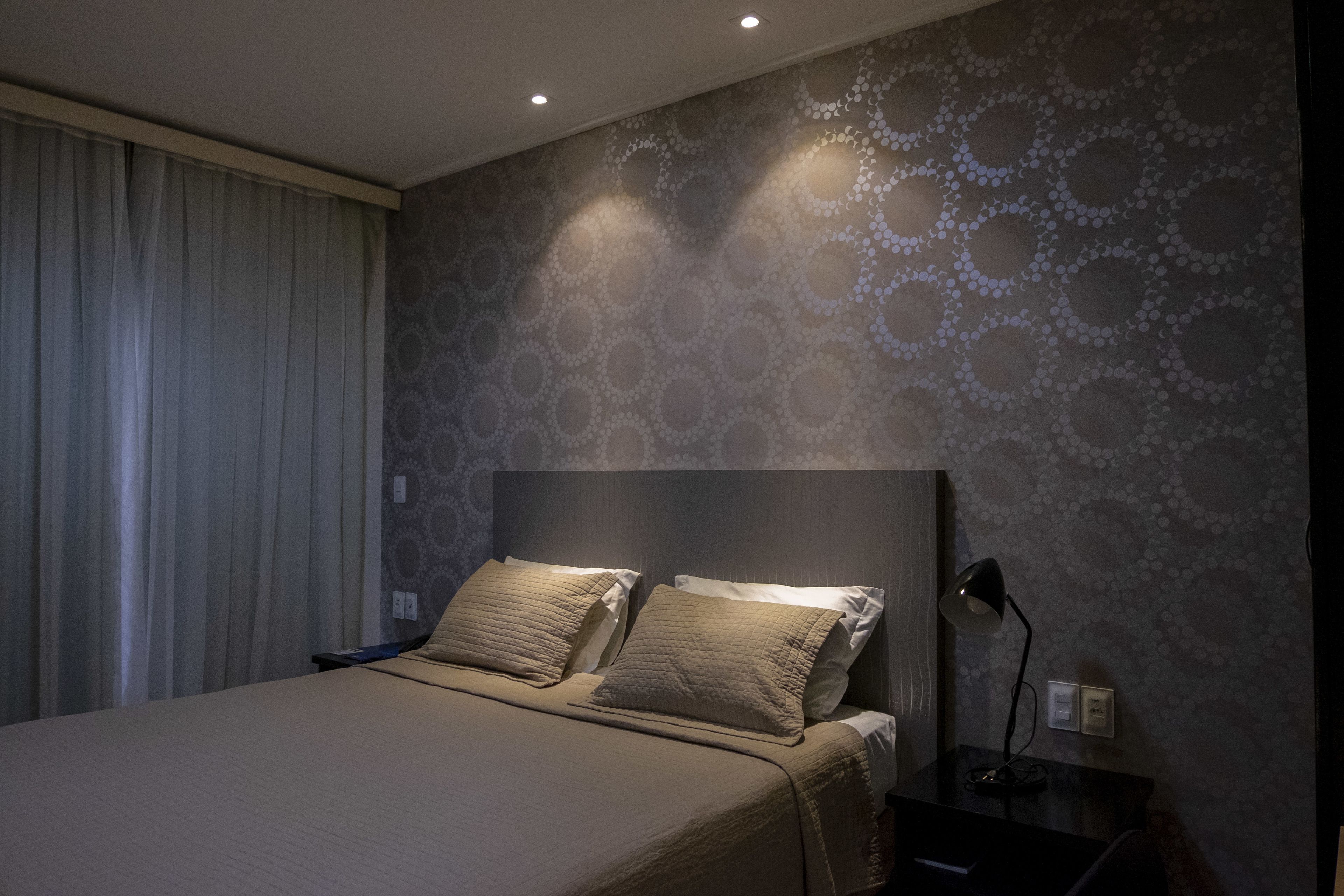 A modern bedroom with a large bed, a headboard, and a nightstand with a lamp.