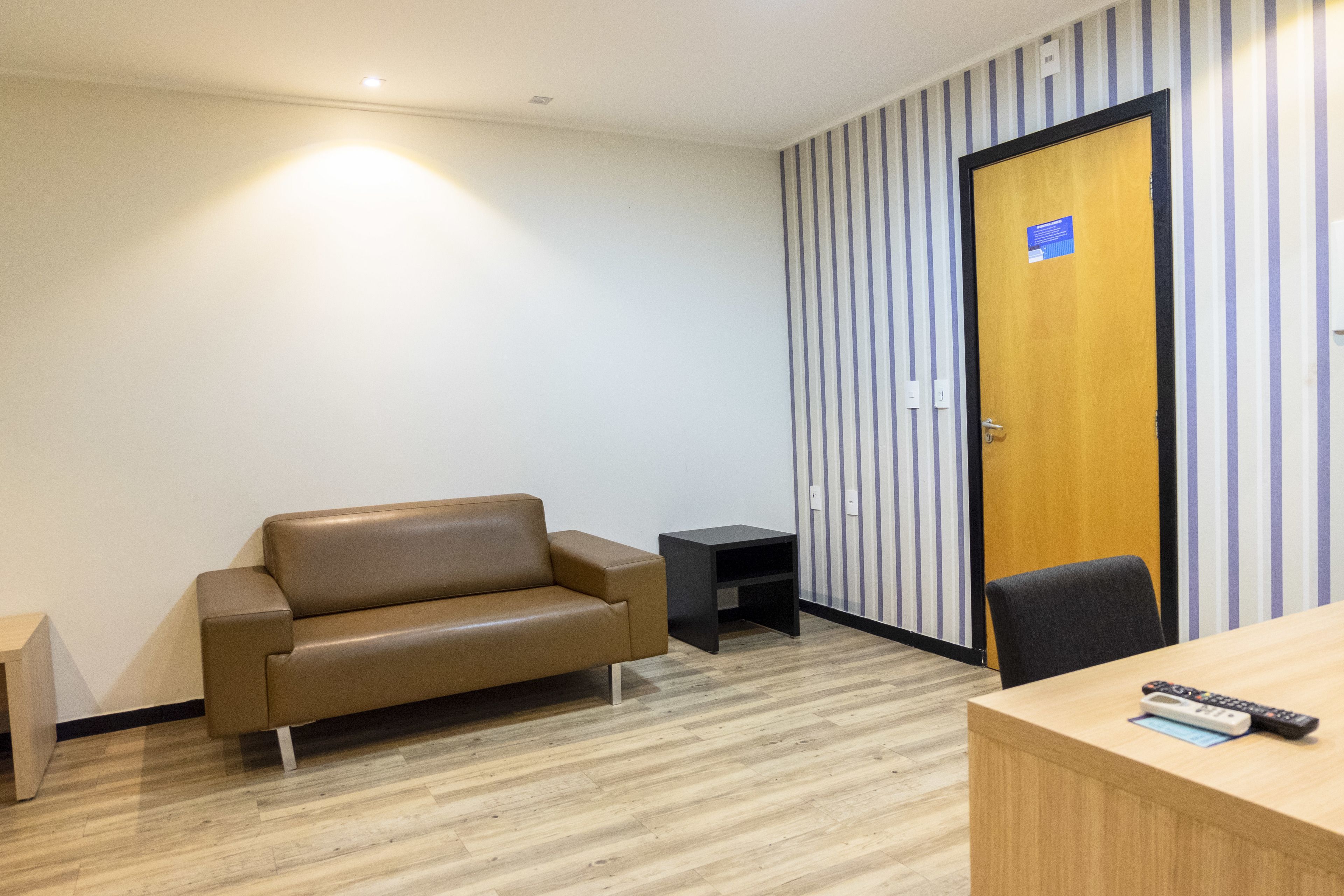 A room with a wooden desk, a brown leather sofa, a small black side table, and a door with a sign.