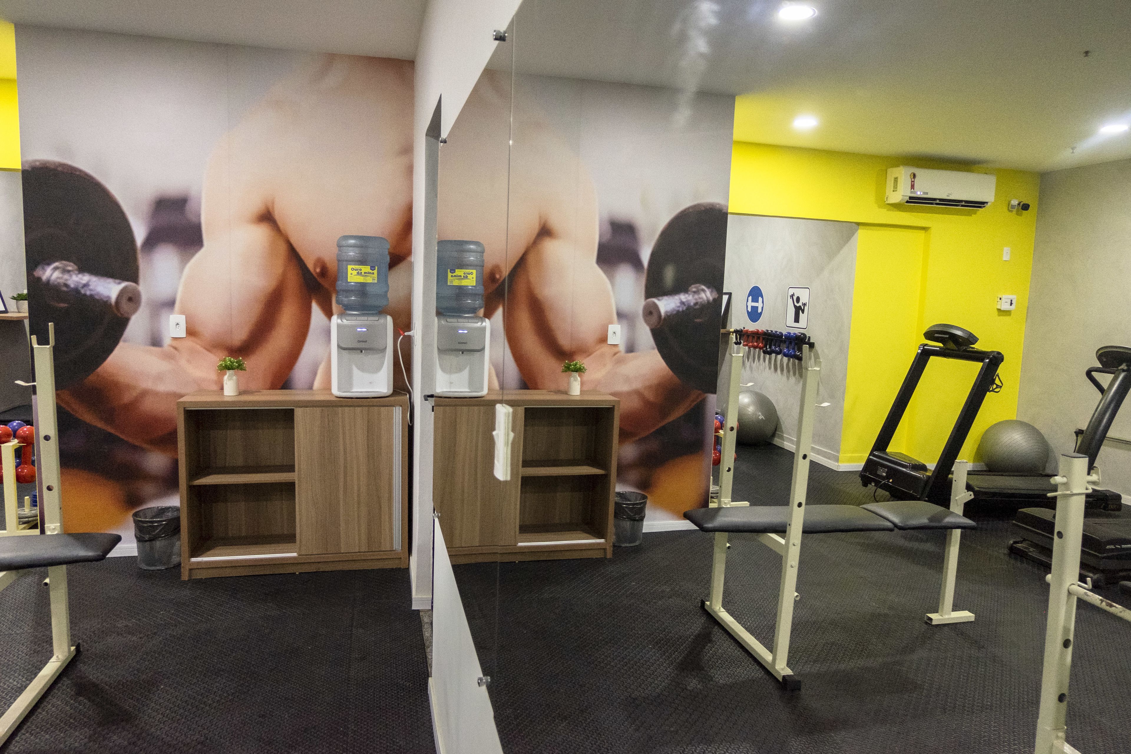 Une salle de sport équipée de matériel d’exercice, de distributeurs d’eau et dotée d’un mur entièrement recouvert de miroirs.