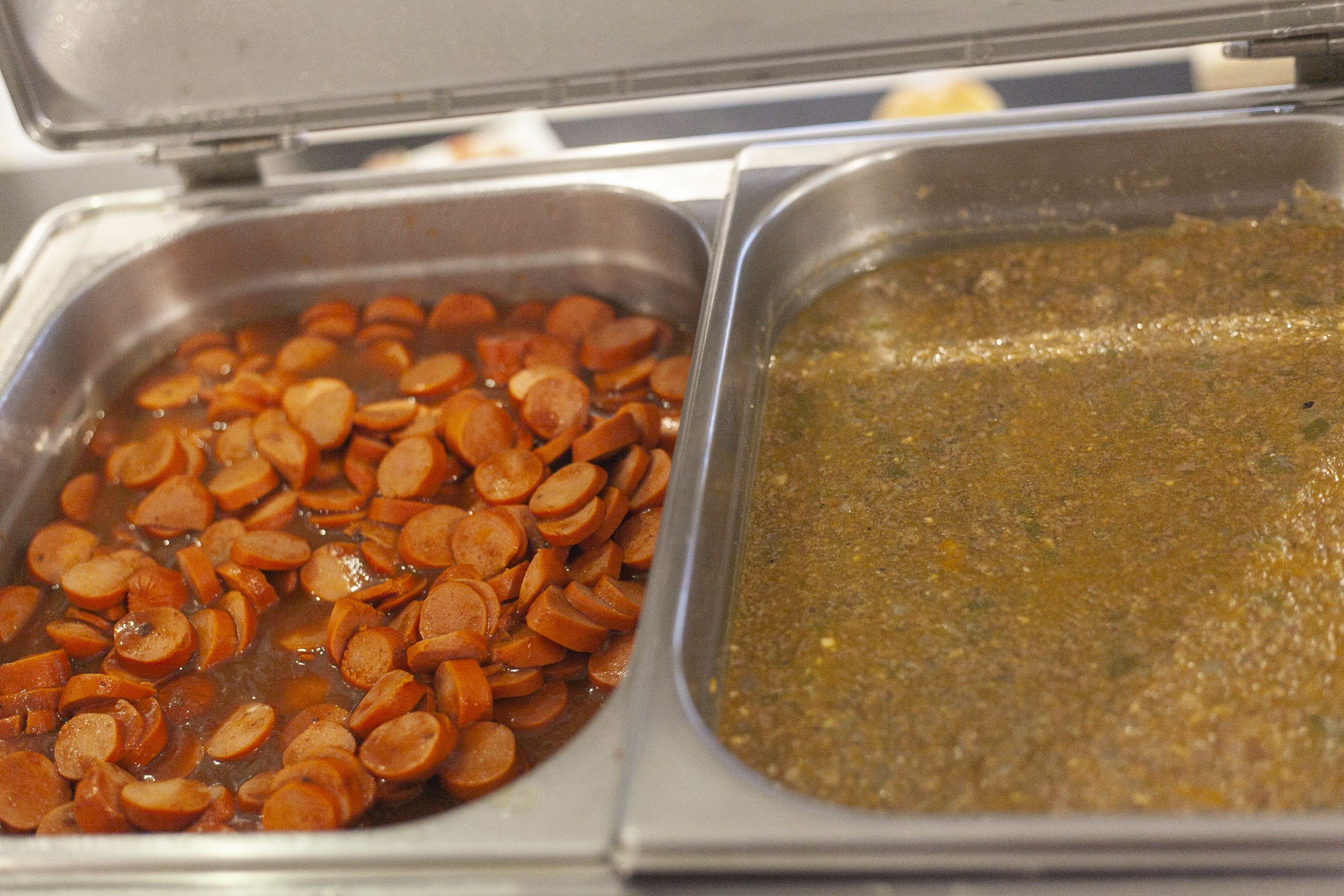 Deux récipients en métal, l’un contenant des tranches de saucisson et l’autre une sauce brune.