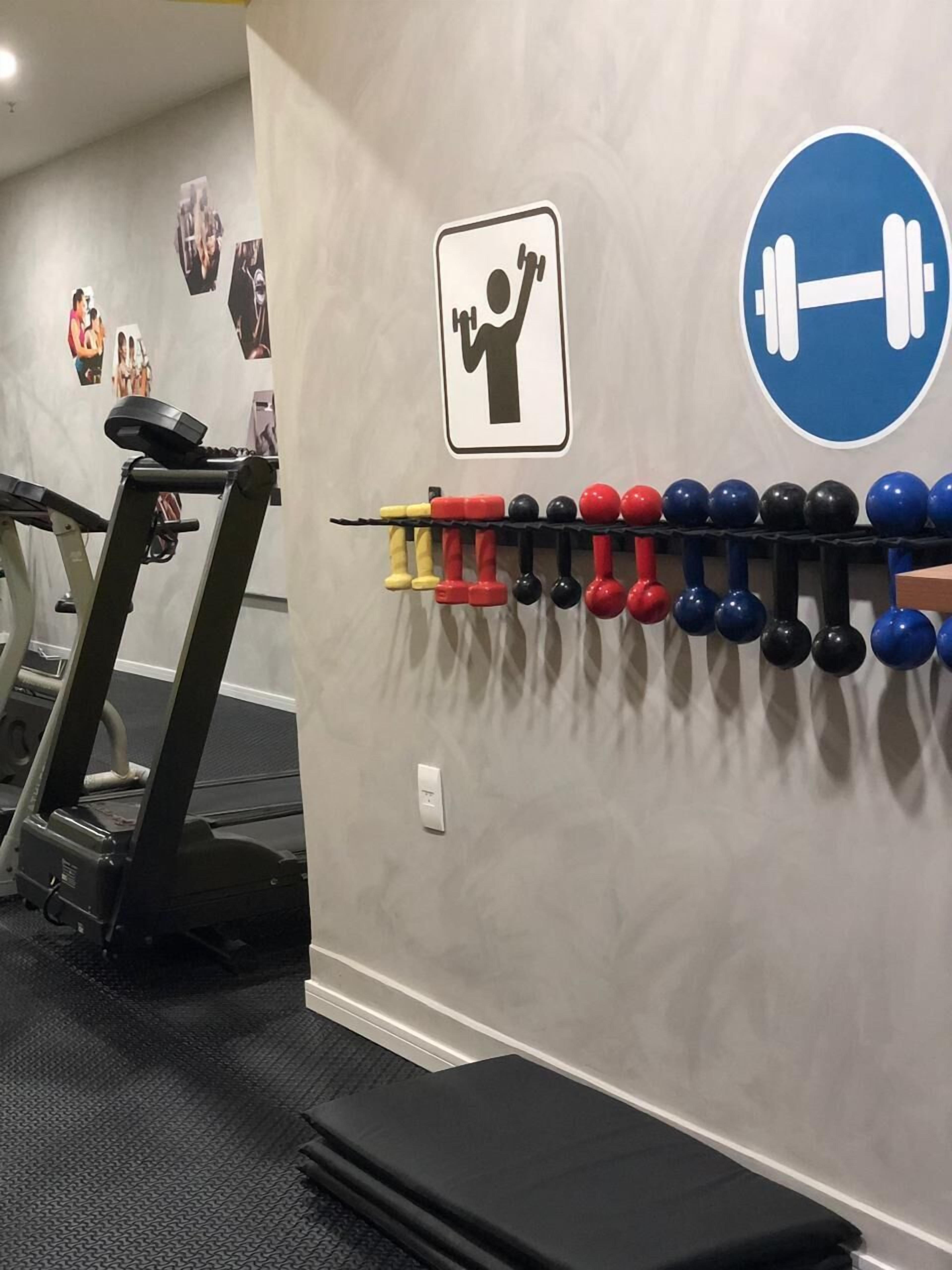Un gimnasio con cinta de correr, mancuernas fijadas a la pared y carteles de ejercicios.