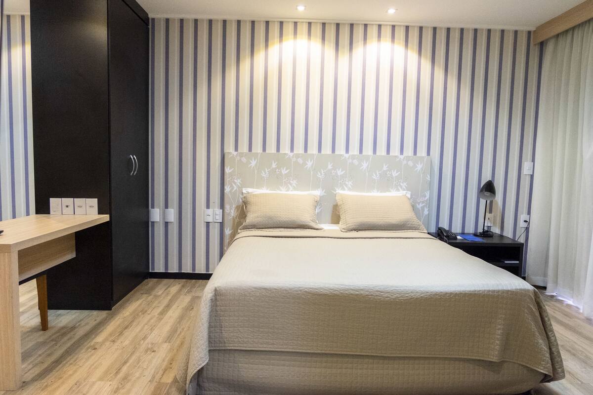 A hotel room with a bed, bedside table, and a desk with a chair.