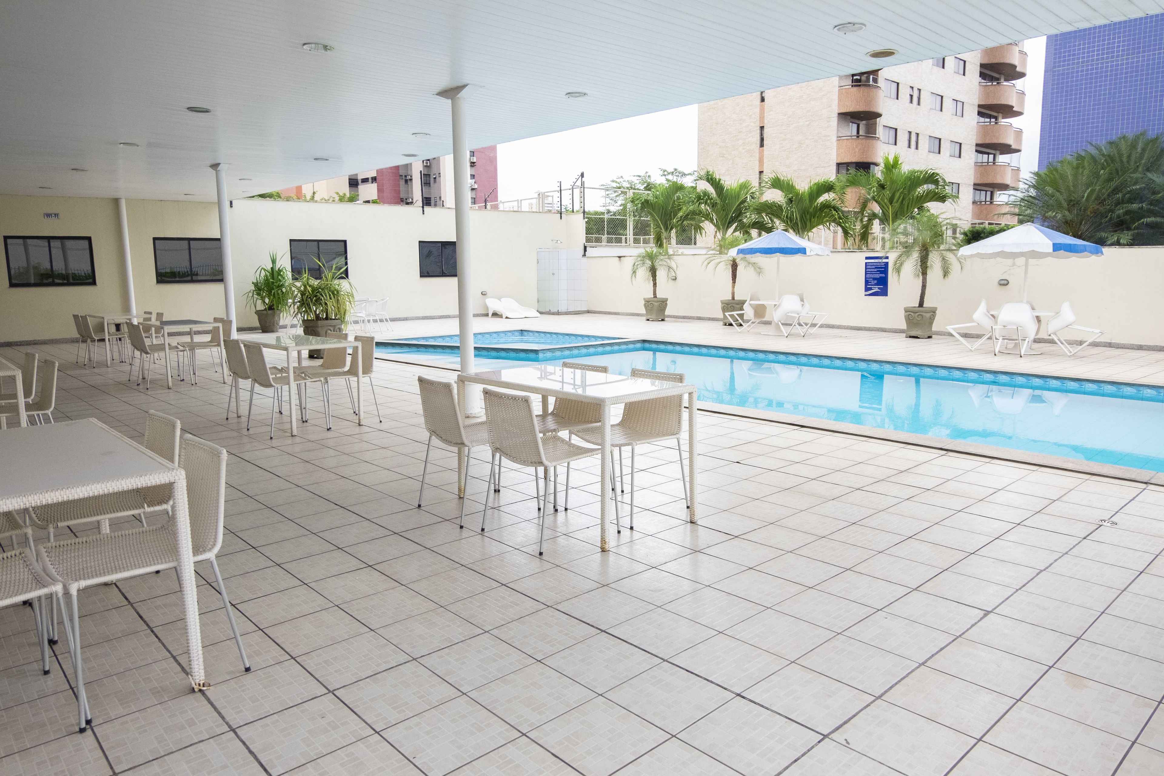 Zona de piscina interior con suelo de baldosas, sillones blancos y mesas.