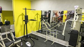 Un gimnasio con diversos equipos de ejercicio, como cintas de correr, máquinas de pesas y una banca.