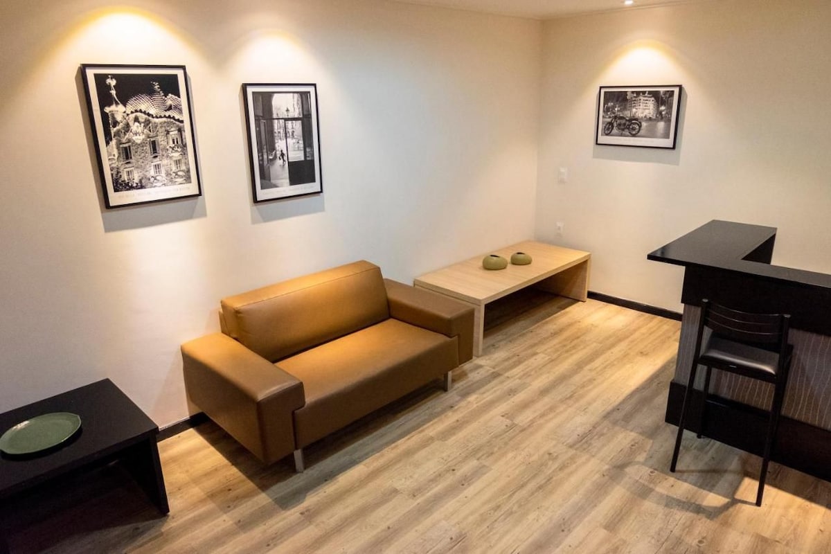 Una sala de estar moderna con un sofá, una mesita y una mesa de centro. Hay cuadros en la pared.
