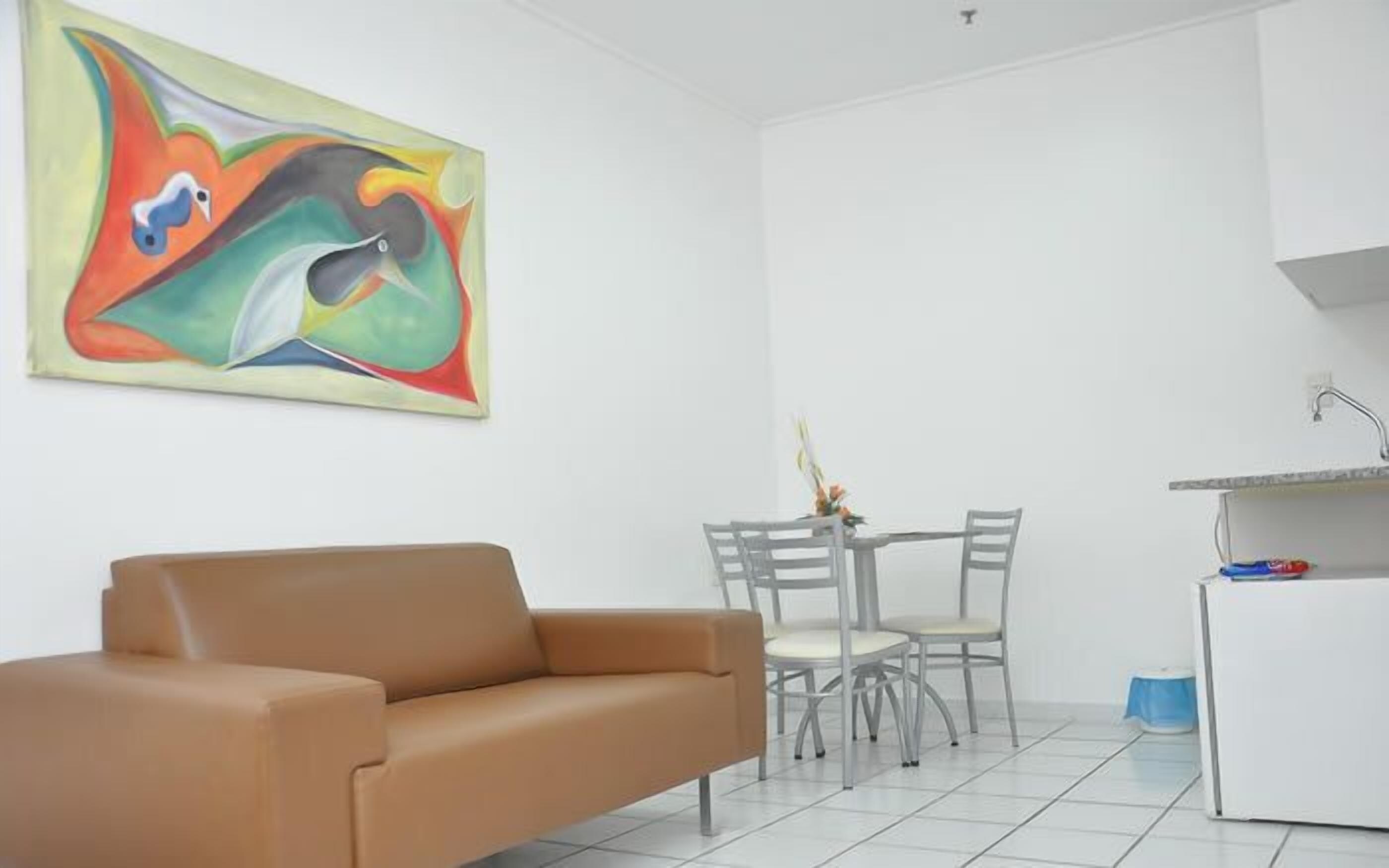 A modern living room with a brown sofa, a dining table with chairs, and a colorful abstract painting on the wall.