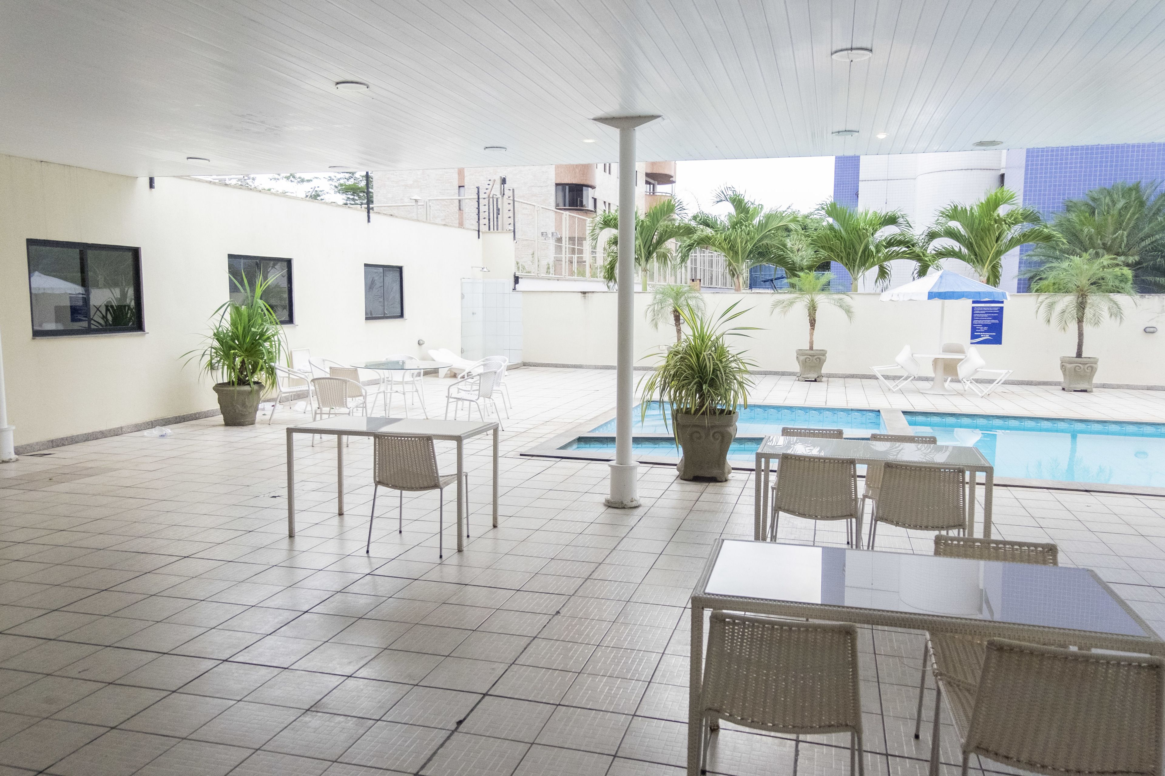 A covered outdoor area with a pool, seating arrangements, and potted plants.