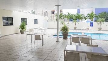 A covered outdoor area with a pool, seating arrangements, and potted plants.