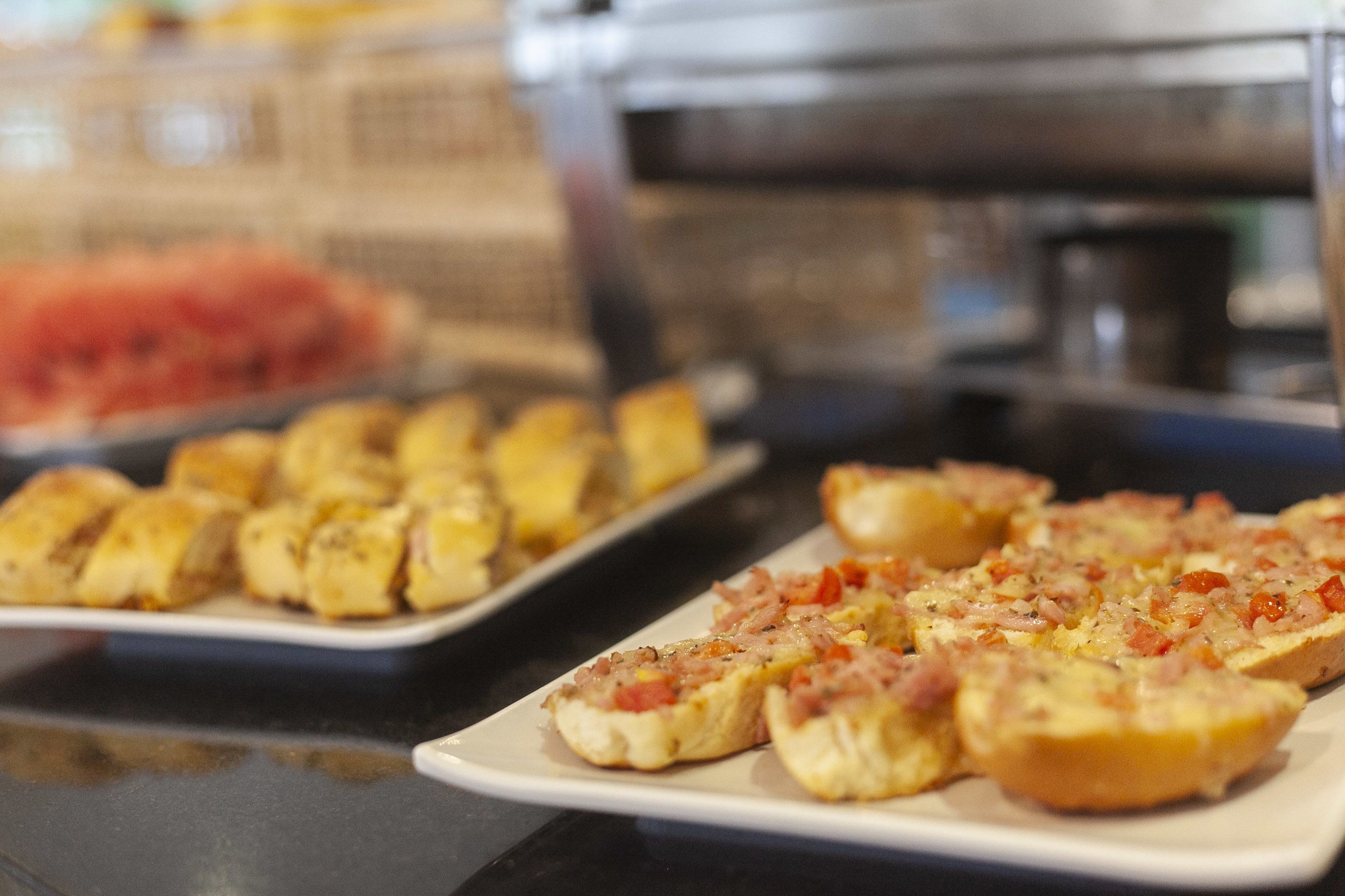 Taula de buffet amb diversos aliments, com ara pans i un plat amb cobertura que sembla formatge i verdures.