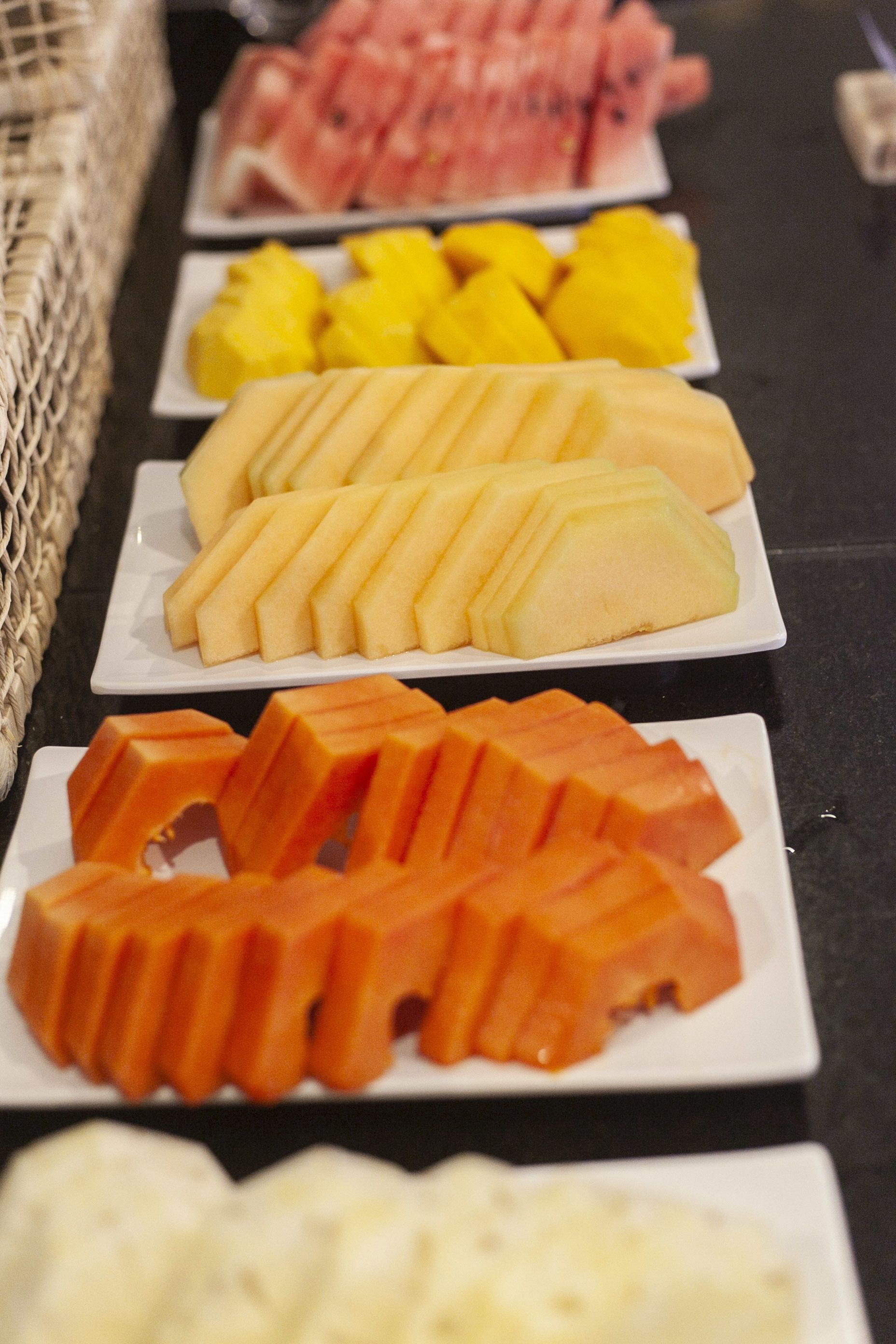 A buffet table with various fruit platters including watermelon, pineapple, cantaloupe, and mango.