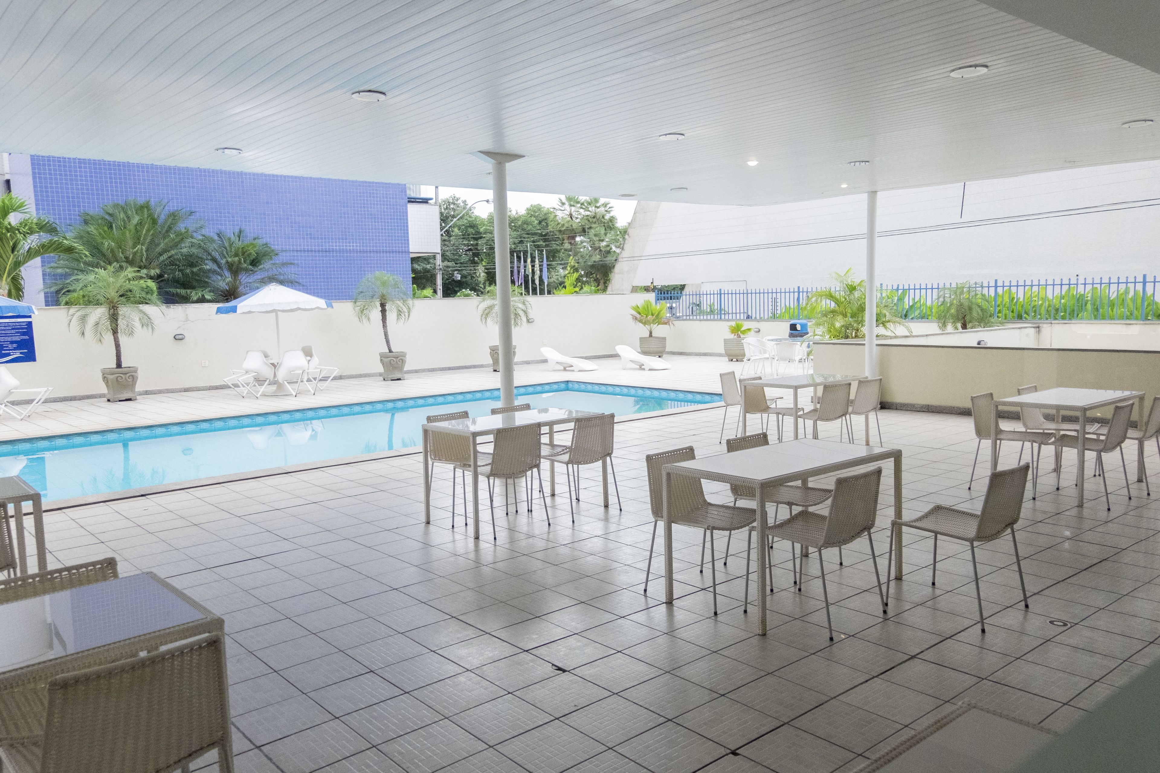 A poolside area with tiled flooring, white lounge chairs, and tables.
