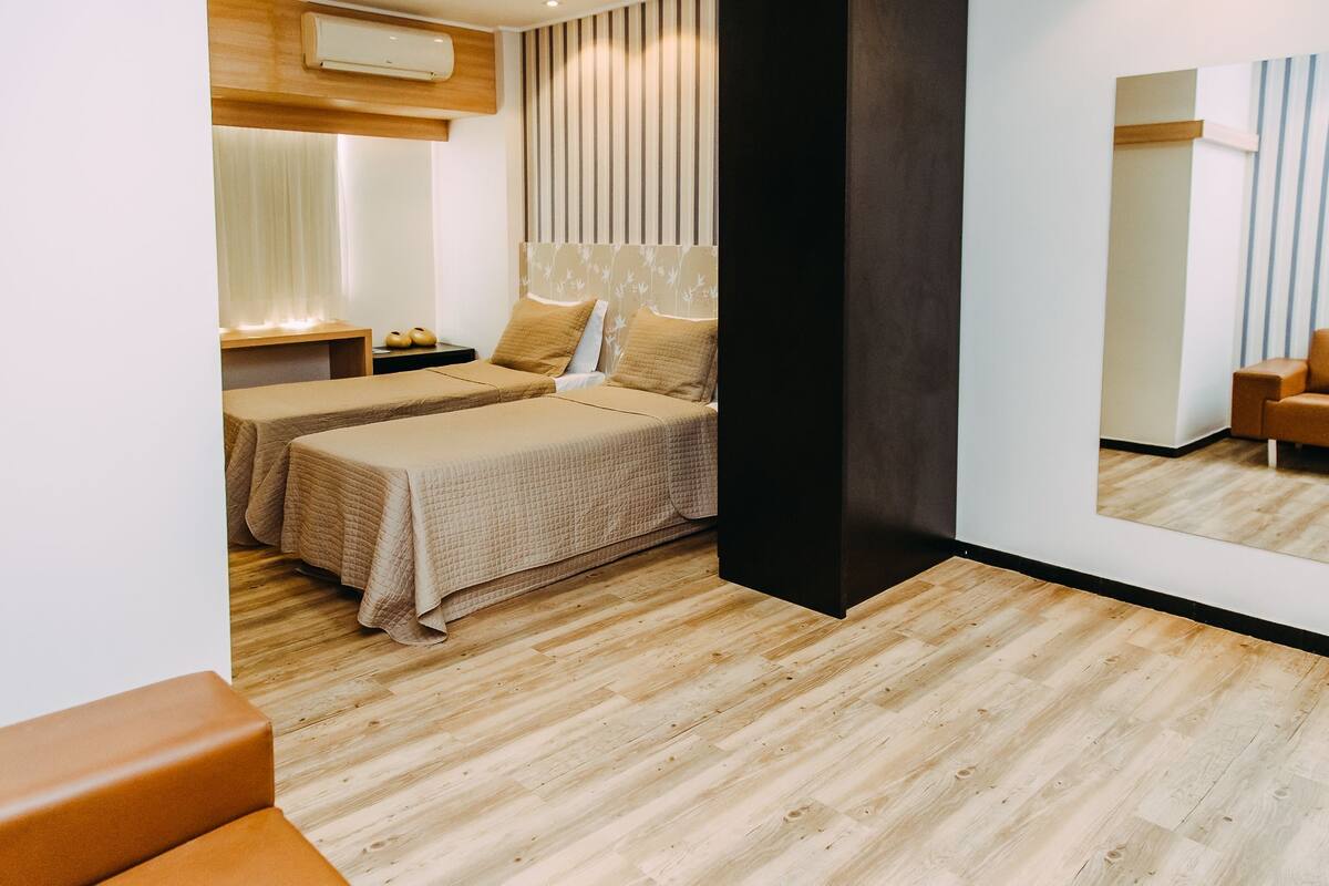 A modern hotel room with two beds, a wooden floor, a large mirror, and a wooden headboard.