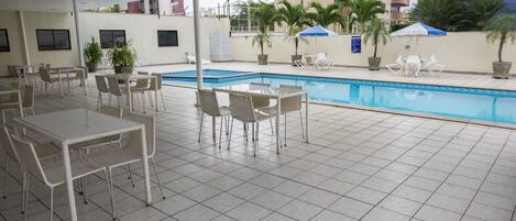 A poolside area with tiled flooring, outdoor seating, and a swimming pool.