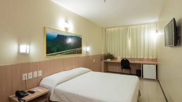 A hotel room with a bed, desk, chair, TV, and a painting on the wall.