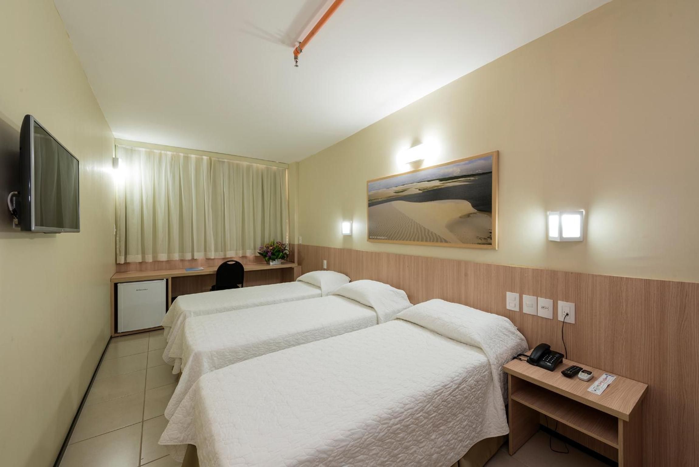A hotel room with two beds, a desk, a television, and a painting on the wall.