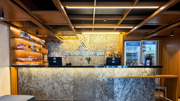 A reception desk with a marble top, wooden shelves with various items, a logo, and a flower arrangement. - Arrey Express Hotel - Teresina (Teresina)