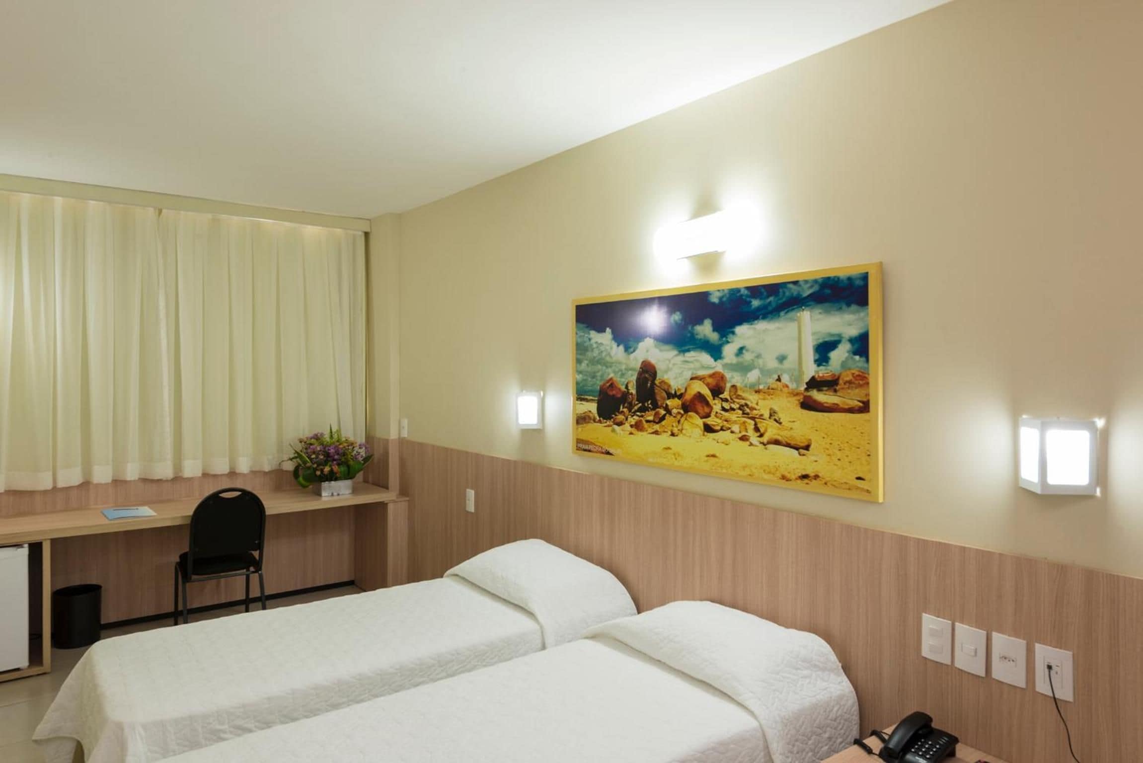 A hotel room with two beds, a desk, a chair, a painting on the wall, and a telephone.