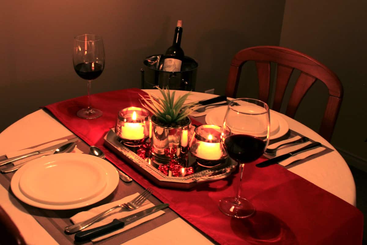 Una mesa de comedor preparada con platos, cubiertos, vasos, velas y una botella de vino.