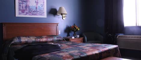 Quarto de hotel com cama, mesa de cabeceira, abajur, cadeira e janela.