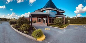 A building with a curved roof and a covered entrance area. - Hôtel Val-des-Sources (Val-des-Sources)