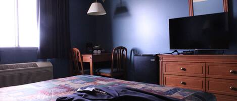 Habitación de hotel con cama, escritorio, silla, cómoda, televisión y ventana con cortinas.