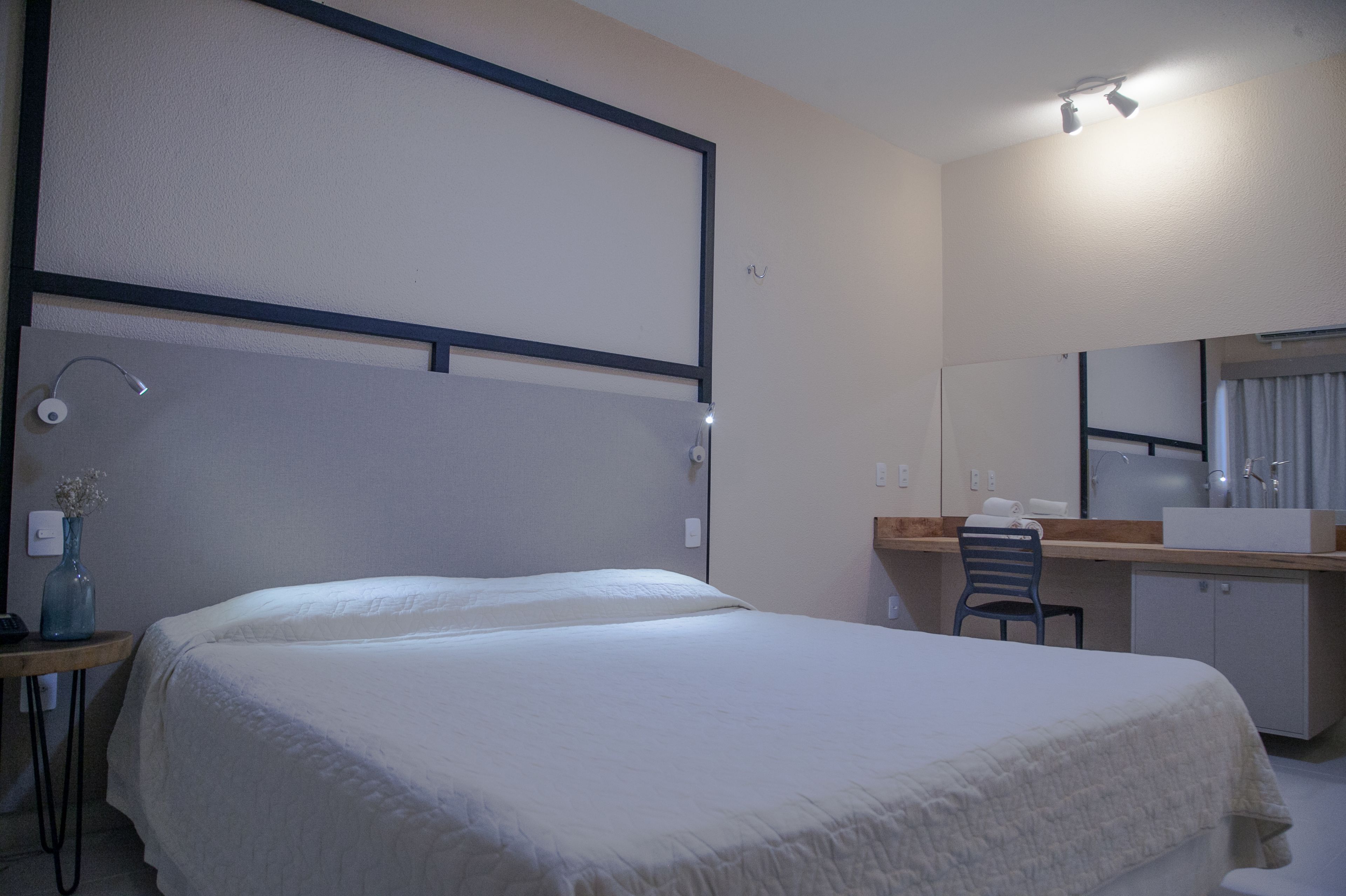 A hotel room with a bed, desk, chair, and a large mirror.