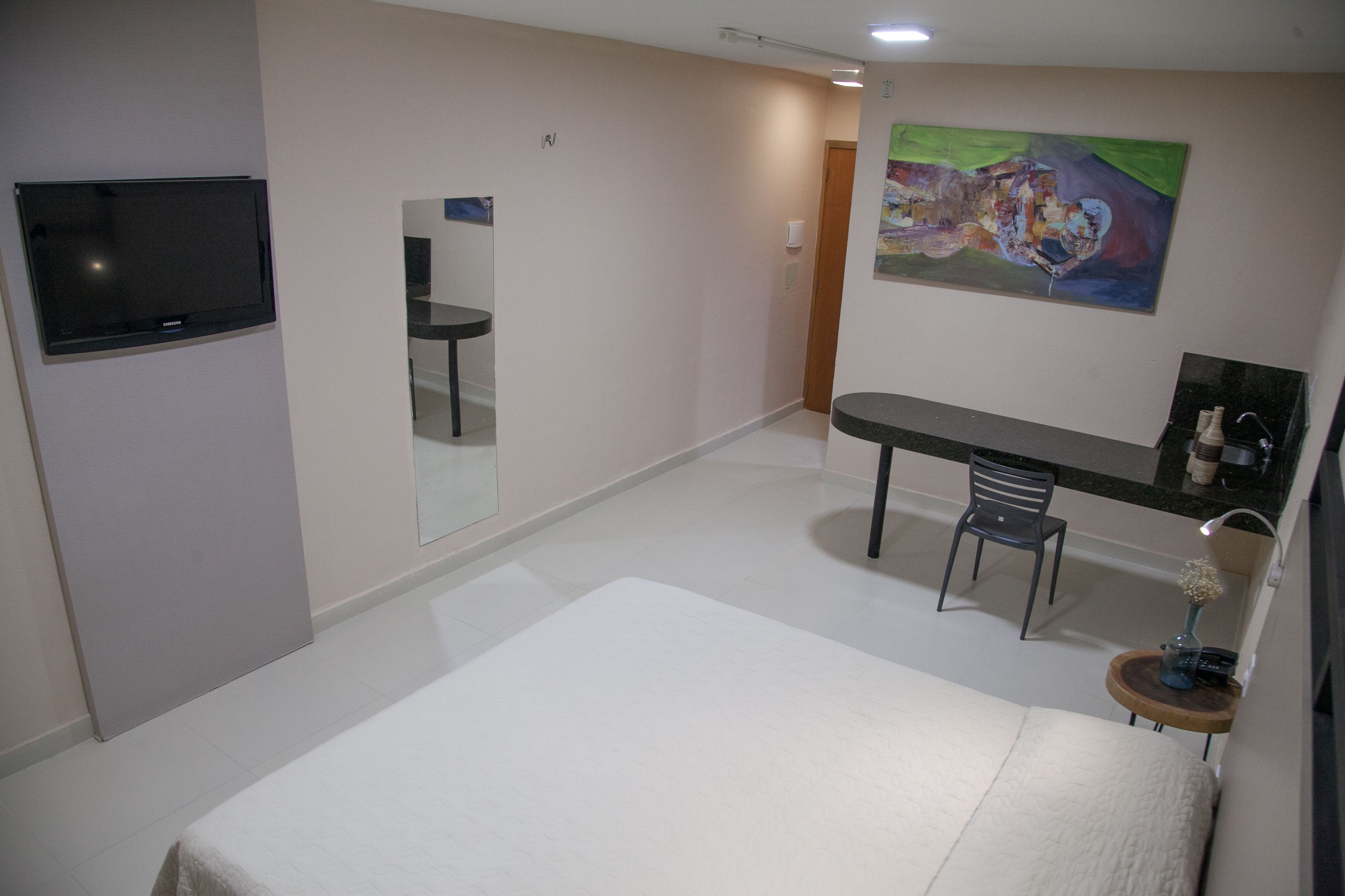 Ein Hotelzimmer mit Bett, Schreibtisch, Stuhl, Fernseher und einem Gemälde an der Wand.