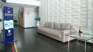A modern lobby with a beige sofa, a glass coffee table, and a geometric patterned wall. A blue sign with white text is visible on the left. - Arrey Fórmula Hotel - Teresina (Teresina)