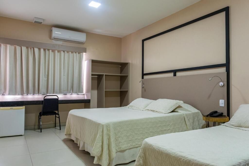 A hotel room with two beds, a desk, a chair, a wardrobe, and a window with curtains.