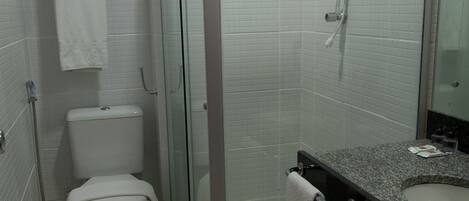 Un baño con inodoro, ducha envuelta en vidrio y lavabo con una toalla colgada al lado.