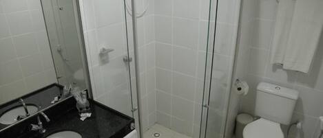 Casa de banho com chuveiro em cabine de vidro, sanita e lavatório com espelho.