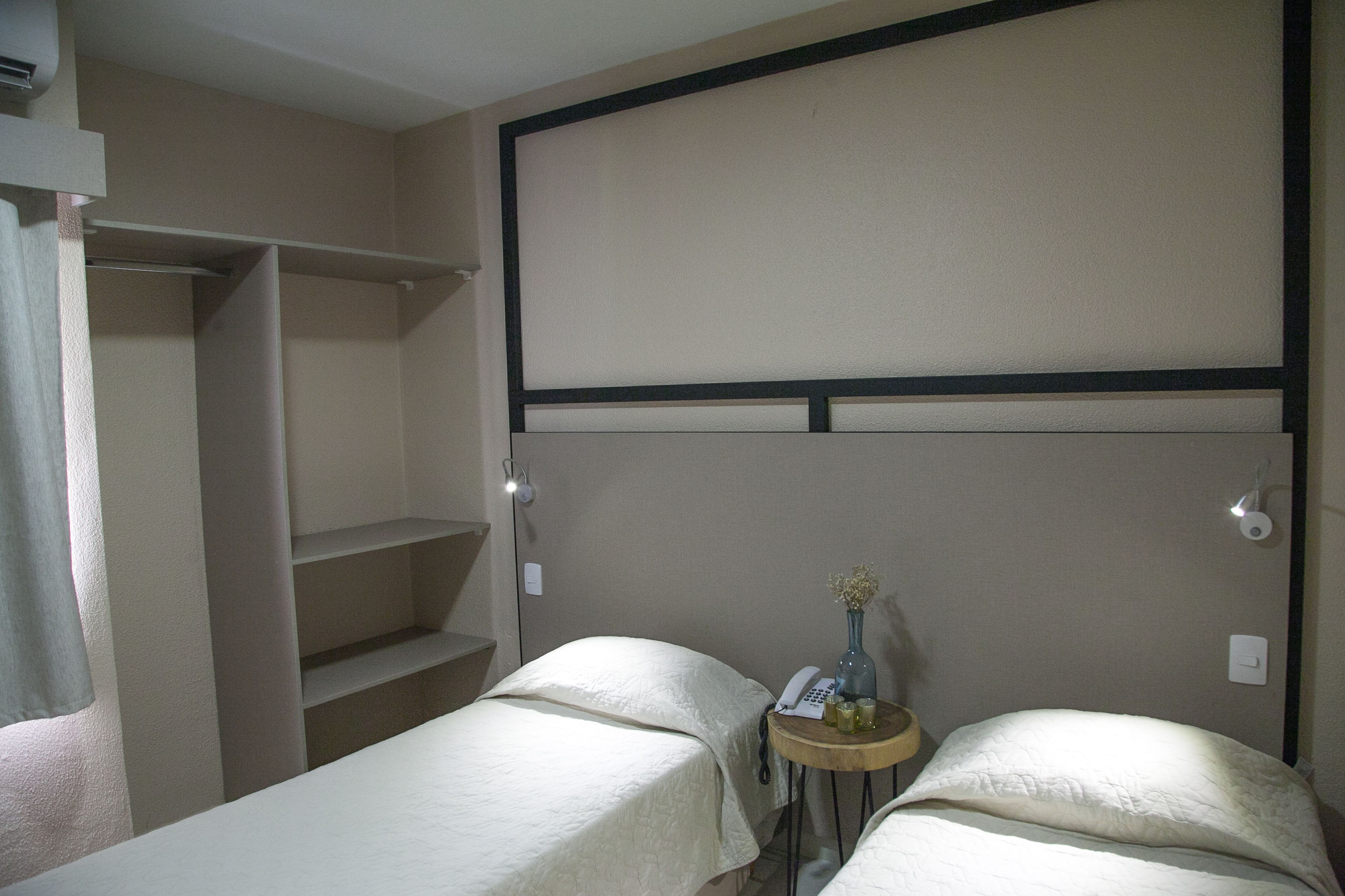 Una habitación de hotel con dos camas, una mesita con un florero y un teléfono, y un armario.