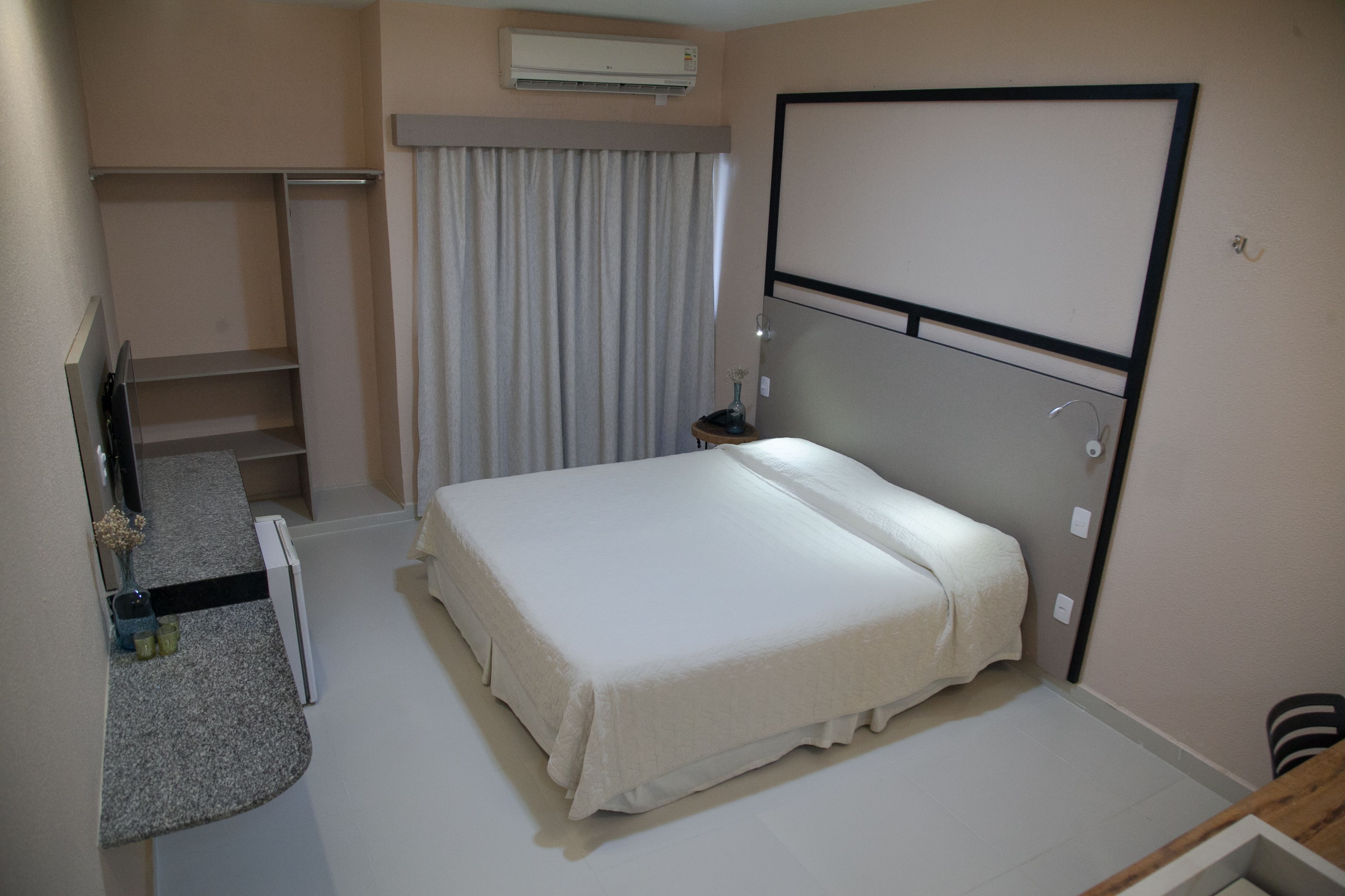 A hotel room with a bed, a desk, a chair, a TV, a wardrobe, and a window with curtains.