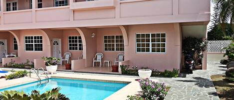 A two-story building with a pool, outdoor seating, and a stone pathway.
