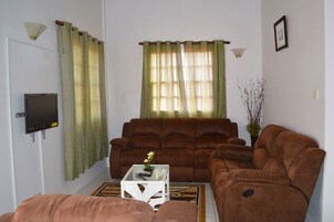 Una sala de estar con un sofá marrón, una mesa de centro blanca y un televisor en la pared.