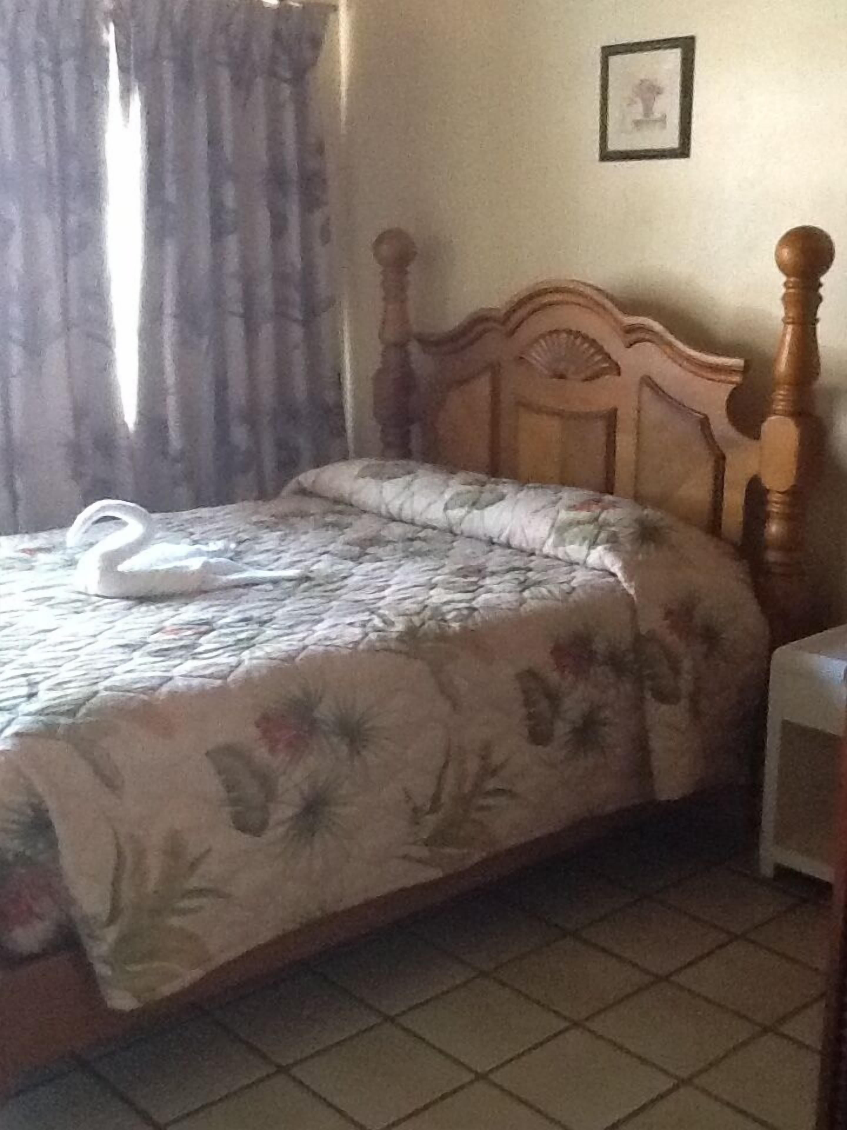 Un dormitorio con estructura de cama de madera, ropa de cama floral, una mesita de noche blanca y un cuadro enmarcado en la pared.