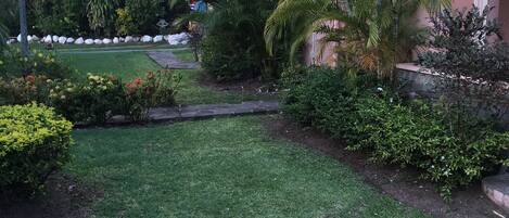 A well-maintained garden with a variety of plants and a stone pathway leading to a building with a pink facade.